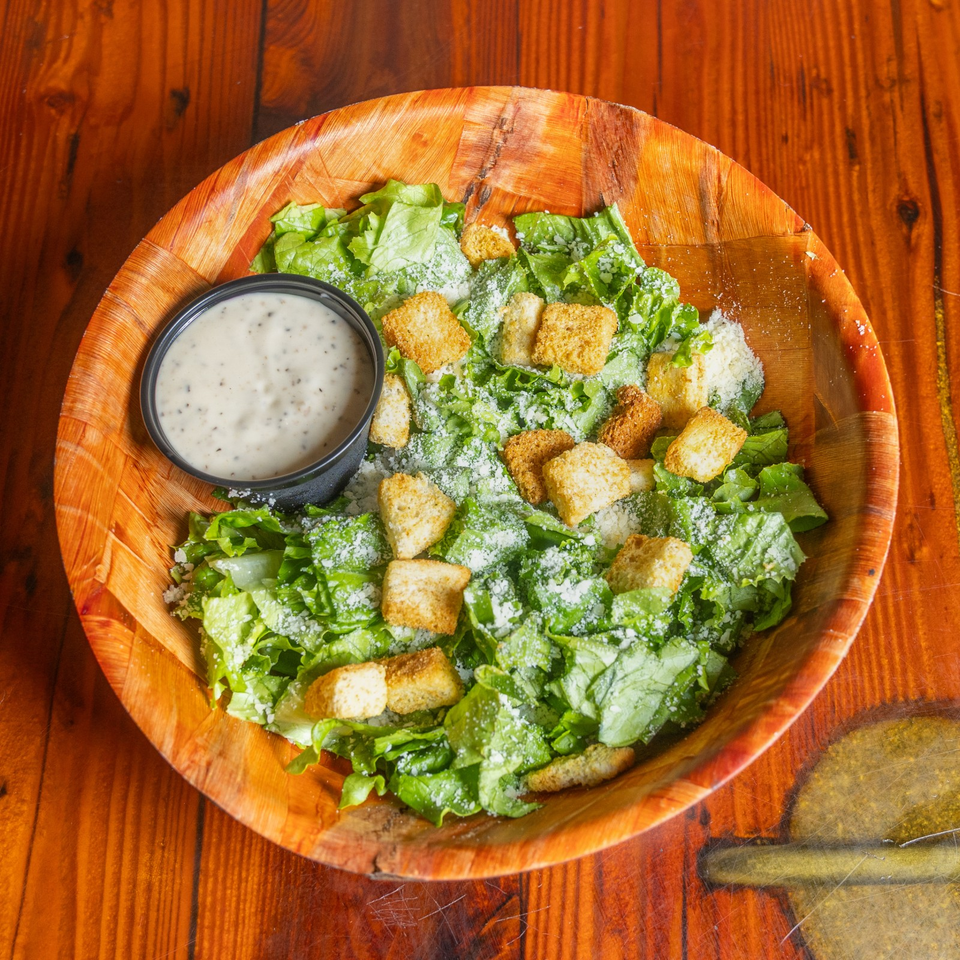Caesar salad with romaine lettuce, croutons, grated cheese, and creamy dressing in a wooden bowl with dipping sauce.